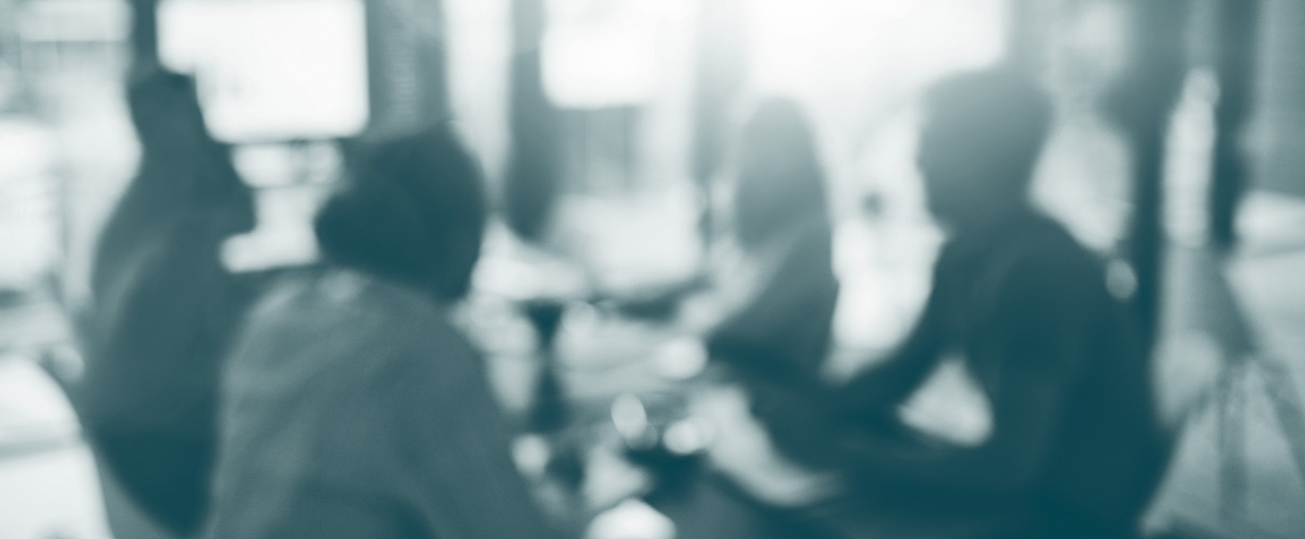 Blurred image of a meeting room with people collaborating around a table, symbolizing teamwork and strategic discussions in a professional setting